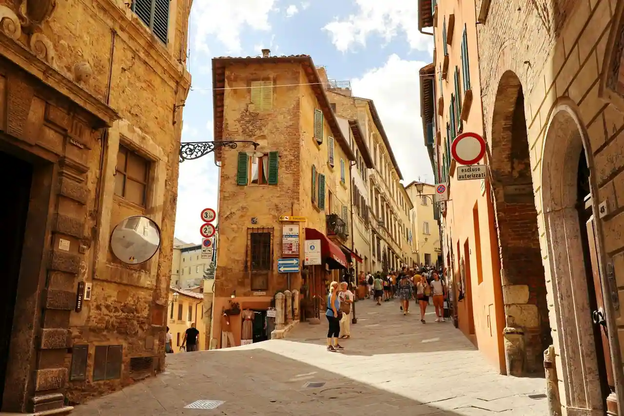 Silhouette féminine en robe de lin écru déambulant dans une rue toscane pavée au soleil de fin d'après-midi