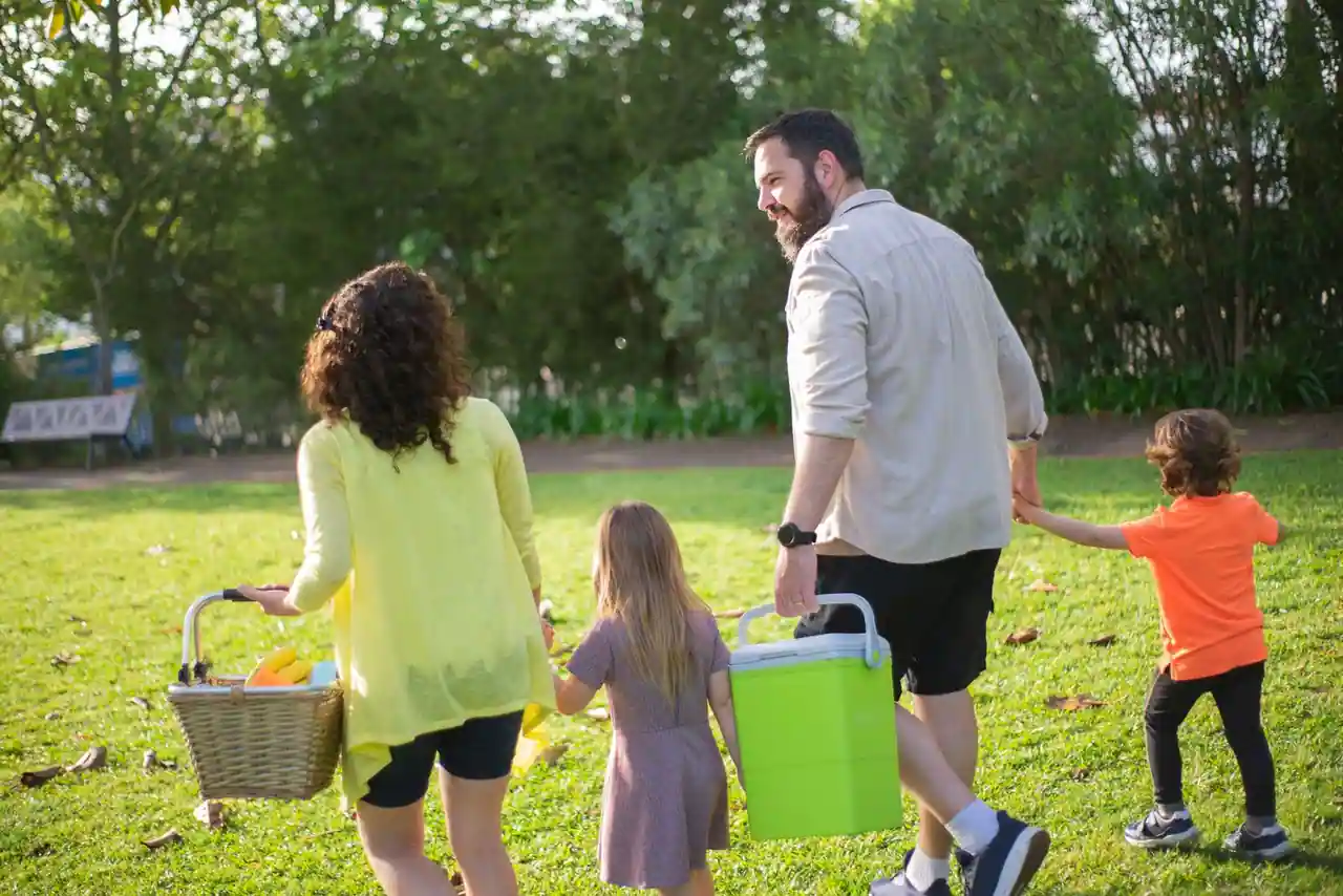 Une famille avec enfants se promène en plein air dans un parc arboré, par une journée ensoleillée.