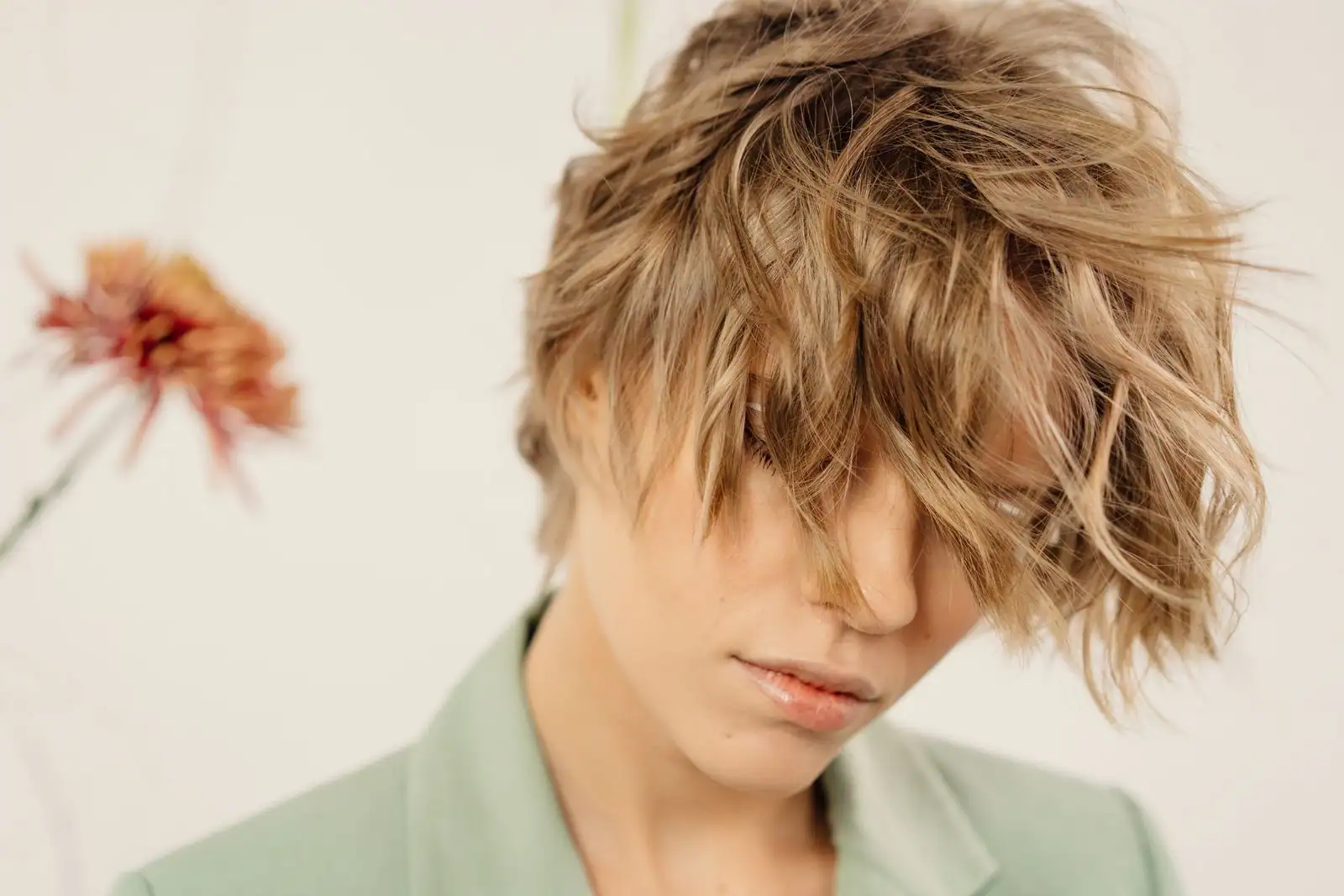Femme à la coupe dégradée et ondulée blond foncé, tête légèrement penchée, sur fond clair