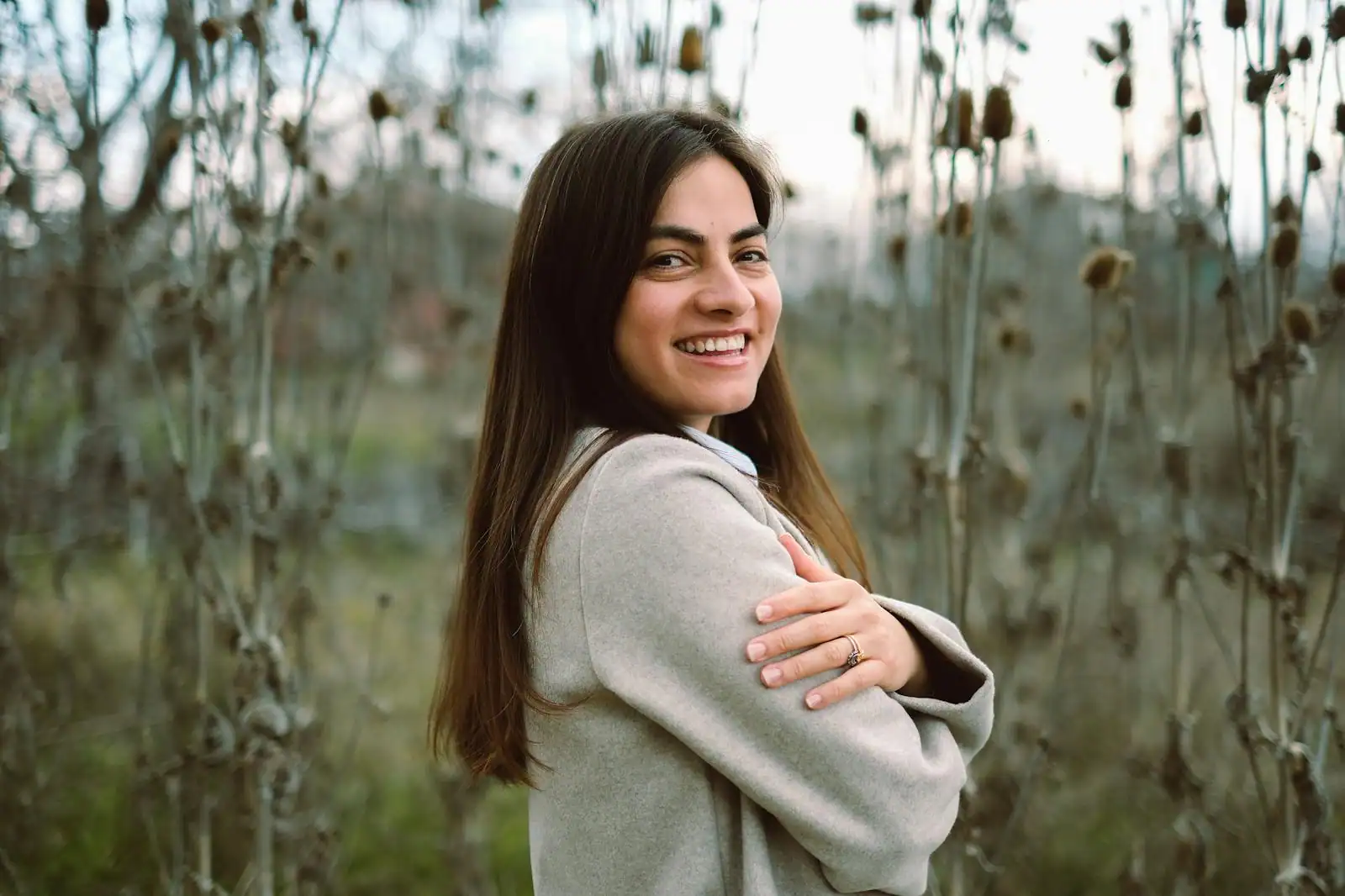 Femme souriante et détendue, debout dans un cadre lumineux, posture assurée et apaisée.