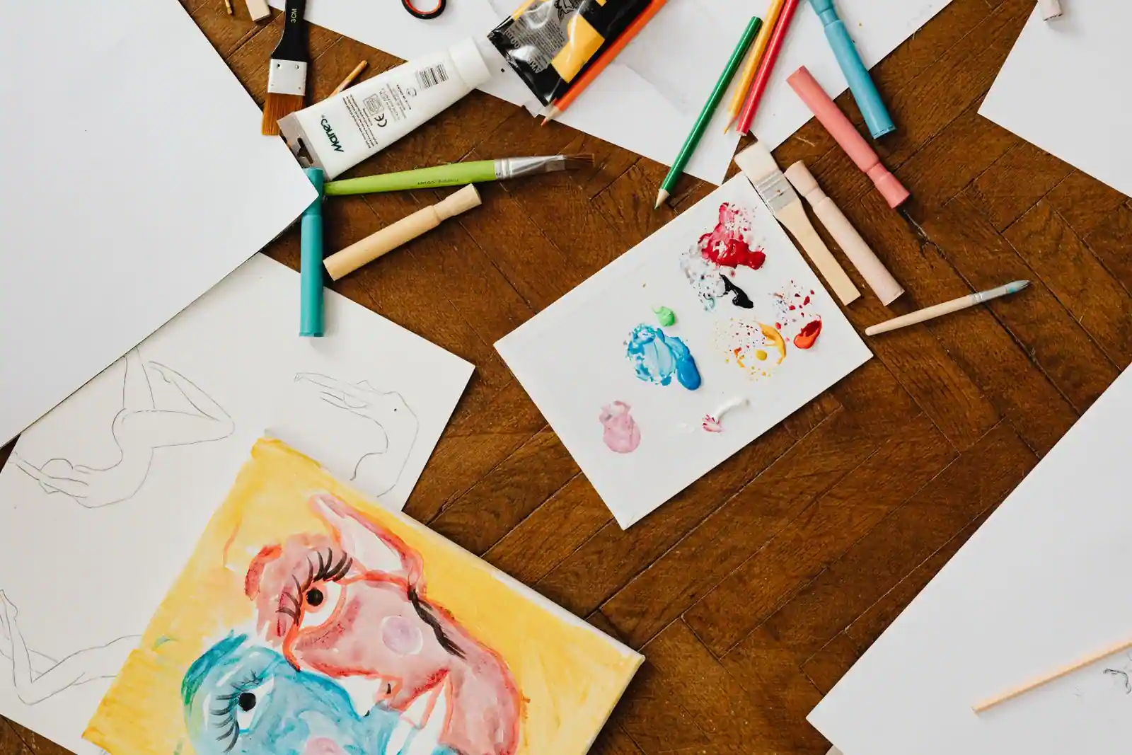 Matériel de dessin et de peinture sur une table en bois : pinceaux, crayons de couleur, feutres et aquarelles.
