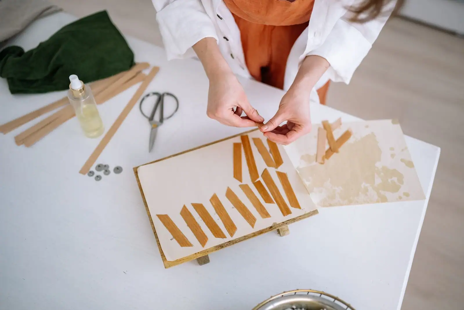 Femme concentrée sur une activité manuelle créative à une table claire, fines lamelles de bois et ciseaux posés autour