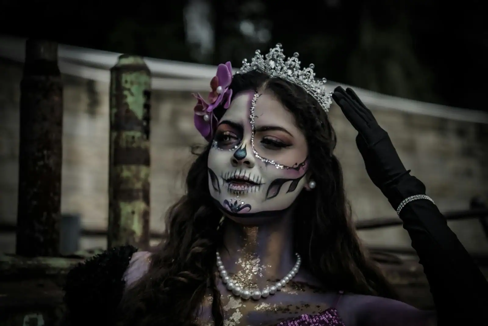 Femme maquillée pour Halloween en tête de mort, visage blanc et orbites noires sur fond sombre