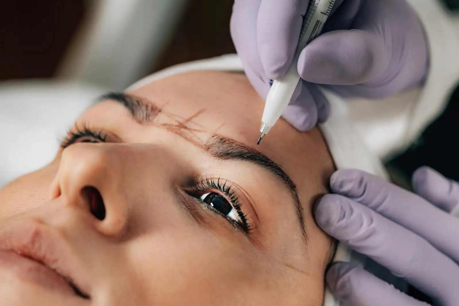 Praticienne réalisant un maquillage permanent des sourcils sur une cliente allongée en institut