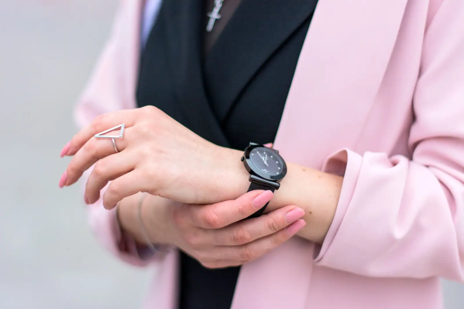 Femme en blazer rose ajustant au poignet sa montre noire minimaliste à bracelet en maille milanaise