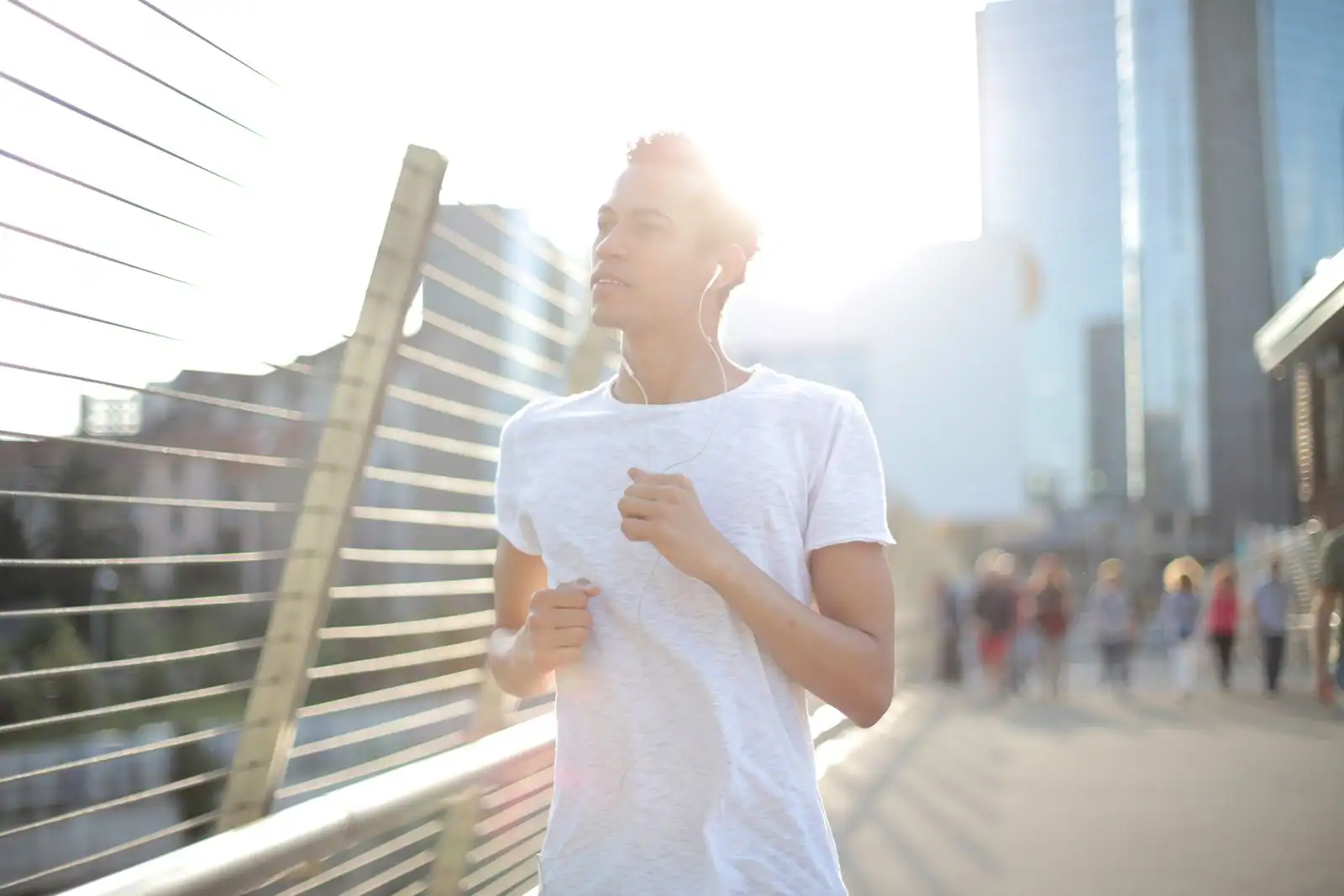 Jeune homme courant sur une passerelle urbaine au lever du soleil, écouteurs aux oreilles.