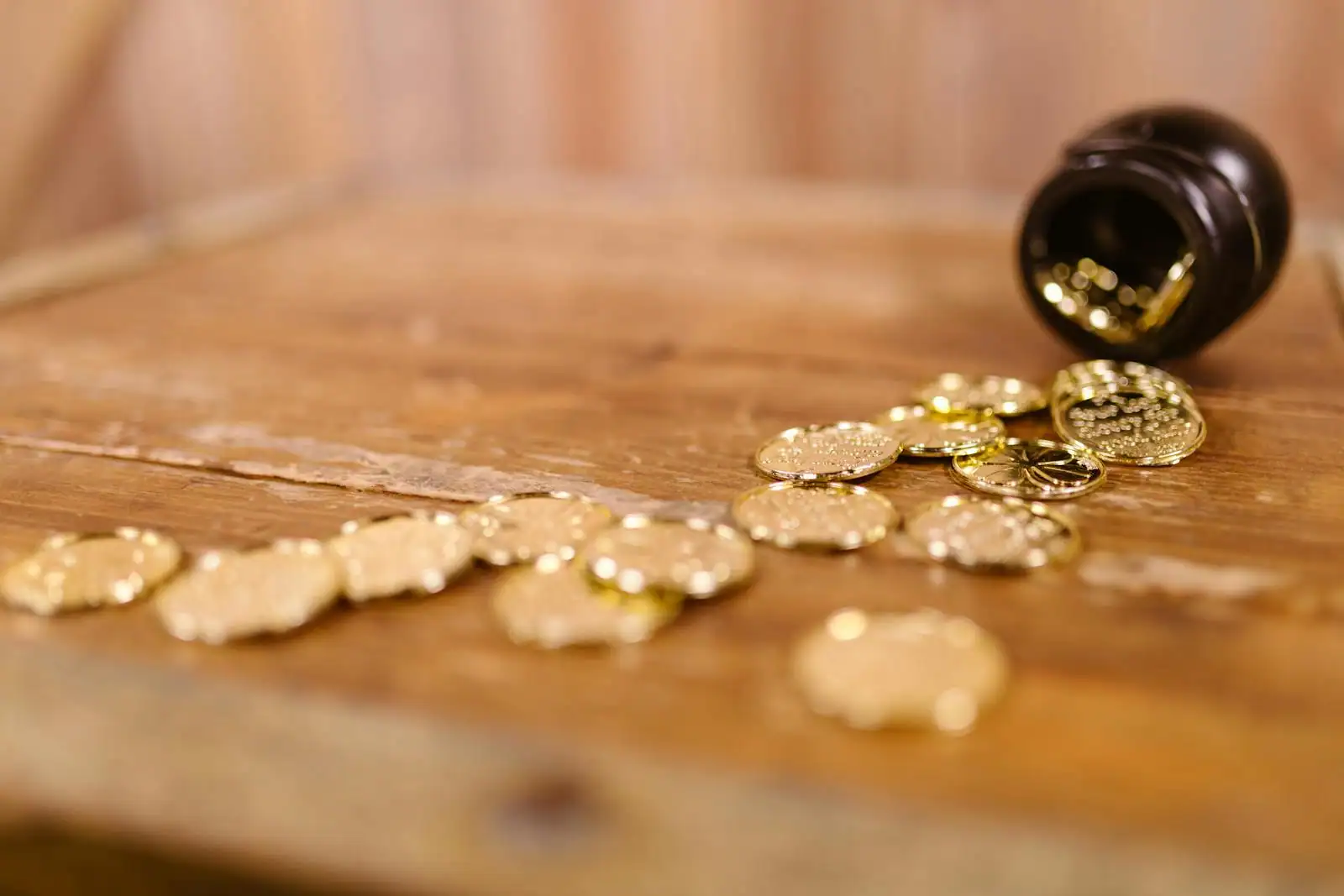 Pièces dorées s'échappant d'un petit pot sombre sur une table en bois, comme un trésor de jeu de salon