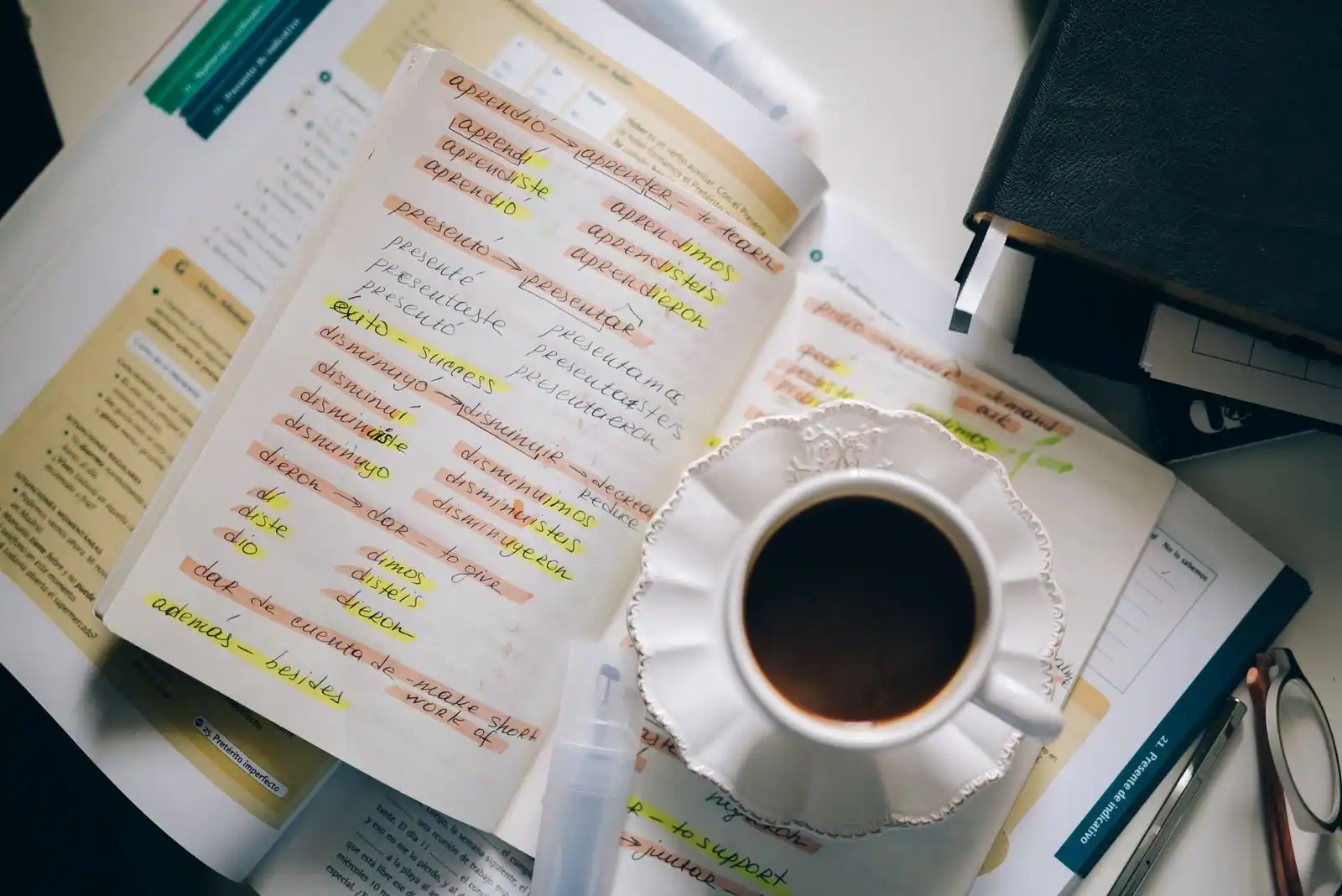 Cahier de notes rempli de conjugaisons espagnoles surlignées, posé près d'une tasse de café pour réviser.