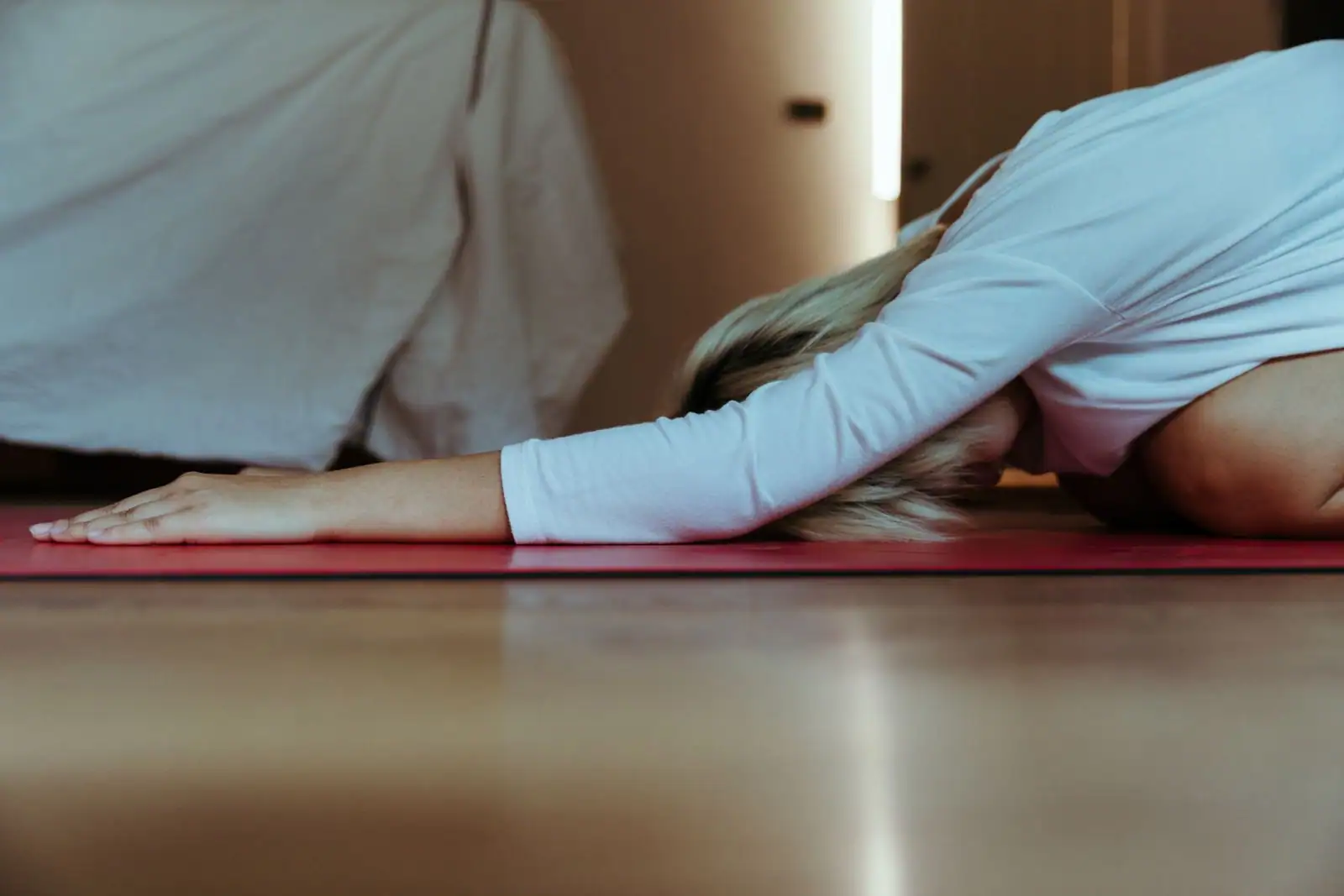 Une personne en posture de yoga repliée vers l'avant sur un tapis rouge, dans une lumière douce.