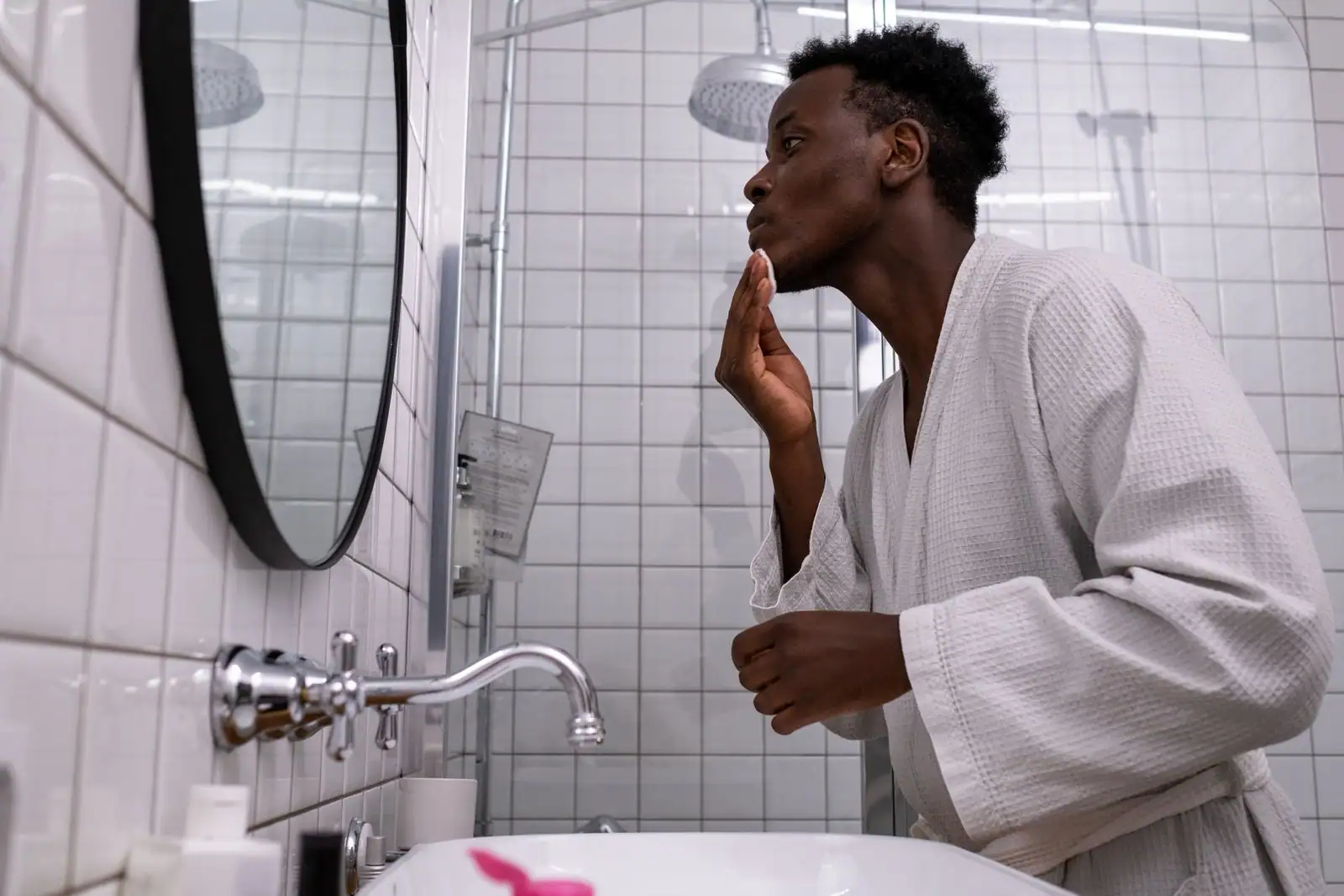 Homme appliquant une crème hydratante sur son visage devant le miroir de la salle de bain