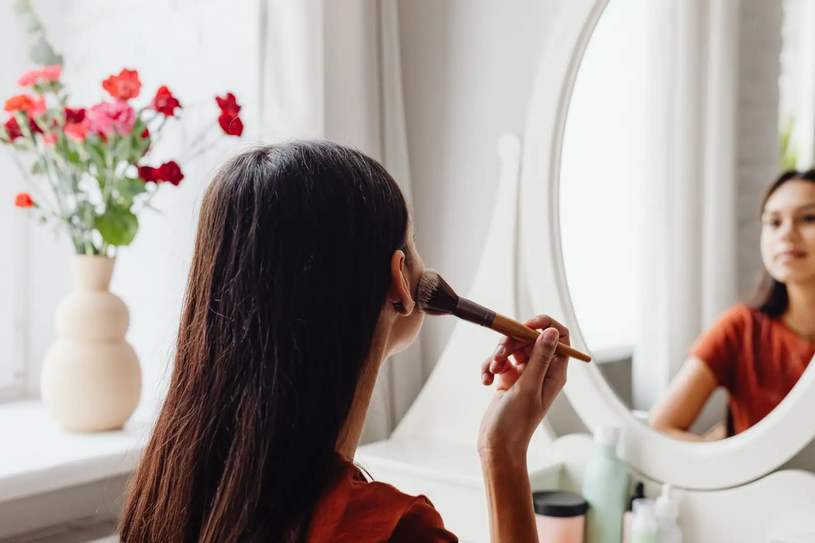 Femme appliquant son maquillage devant un miroir à la lumière naturelle
