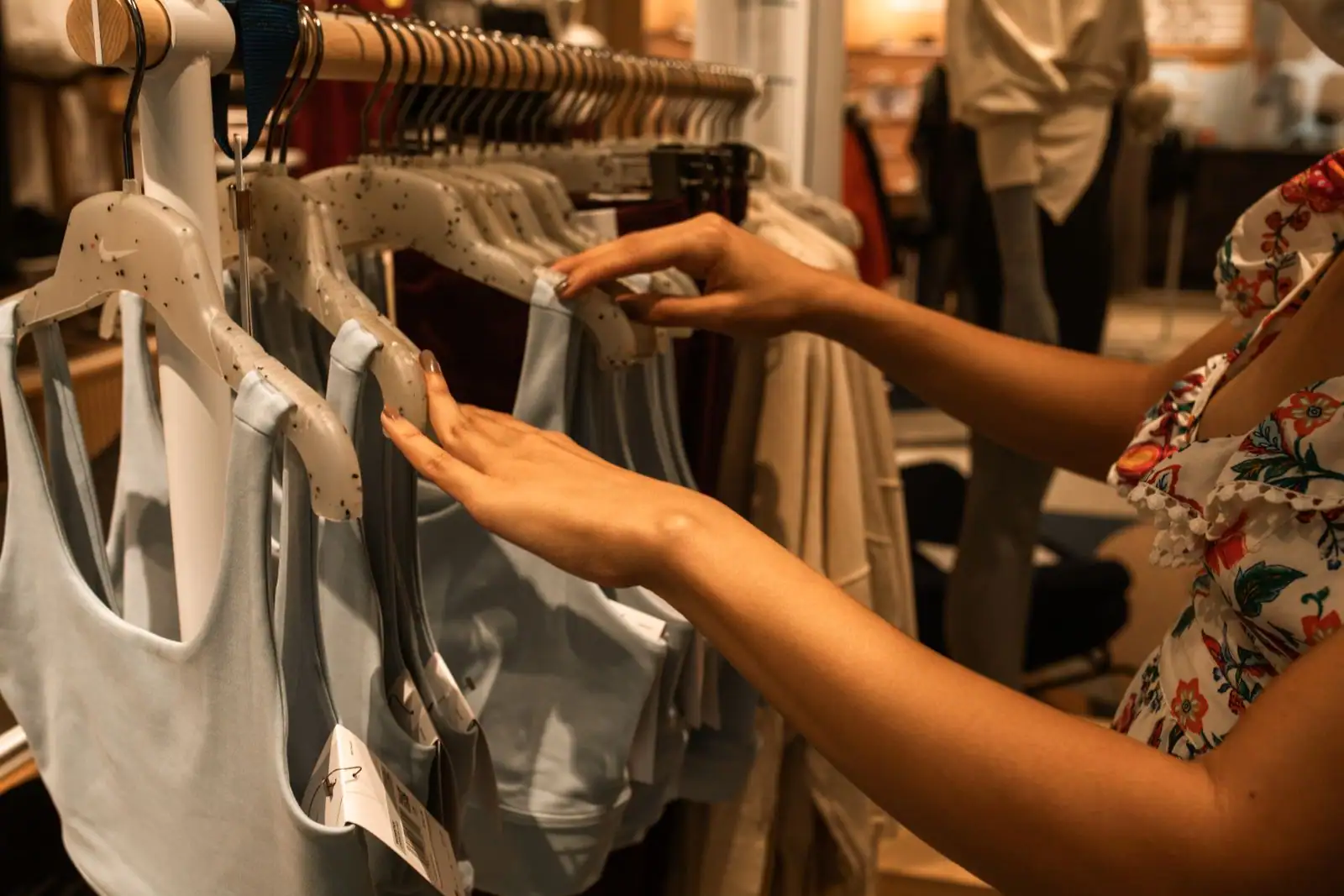 Portant de vêtements féminins dans une boutique de mode, une main parcourt les pièces suspendues.