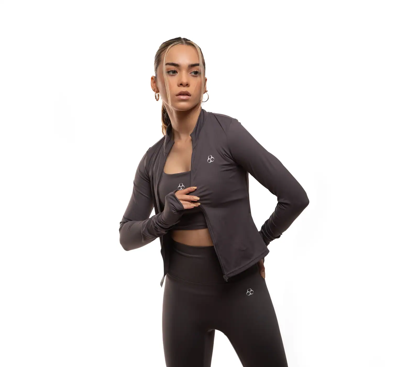 Femme en tenue de sport gris anthracite : veste zippée, brassière et legging assortis, en studio.