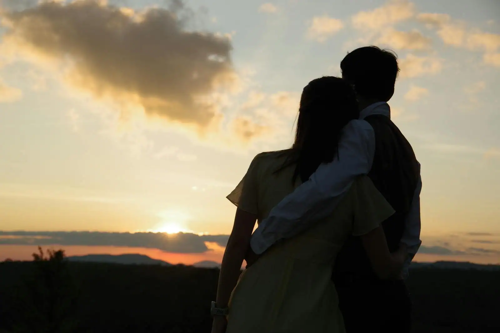 Couple enlacé regardant au loin, silhouettes à contre-jour au coucher du soleil