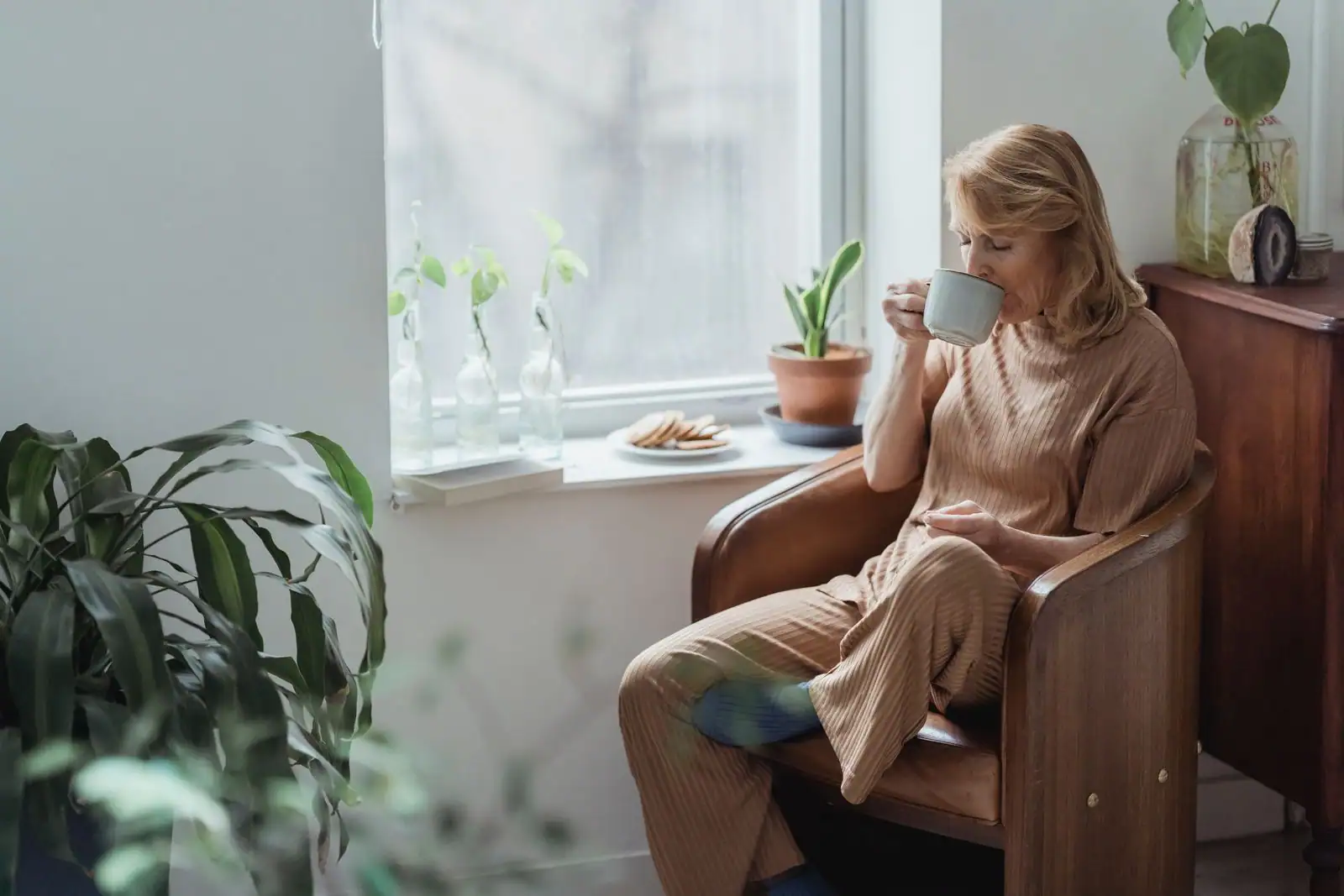 Femme assise près d'une fenêtre, une tasse à la main, dans un intérieur calme et lumineux