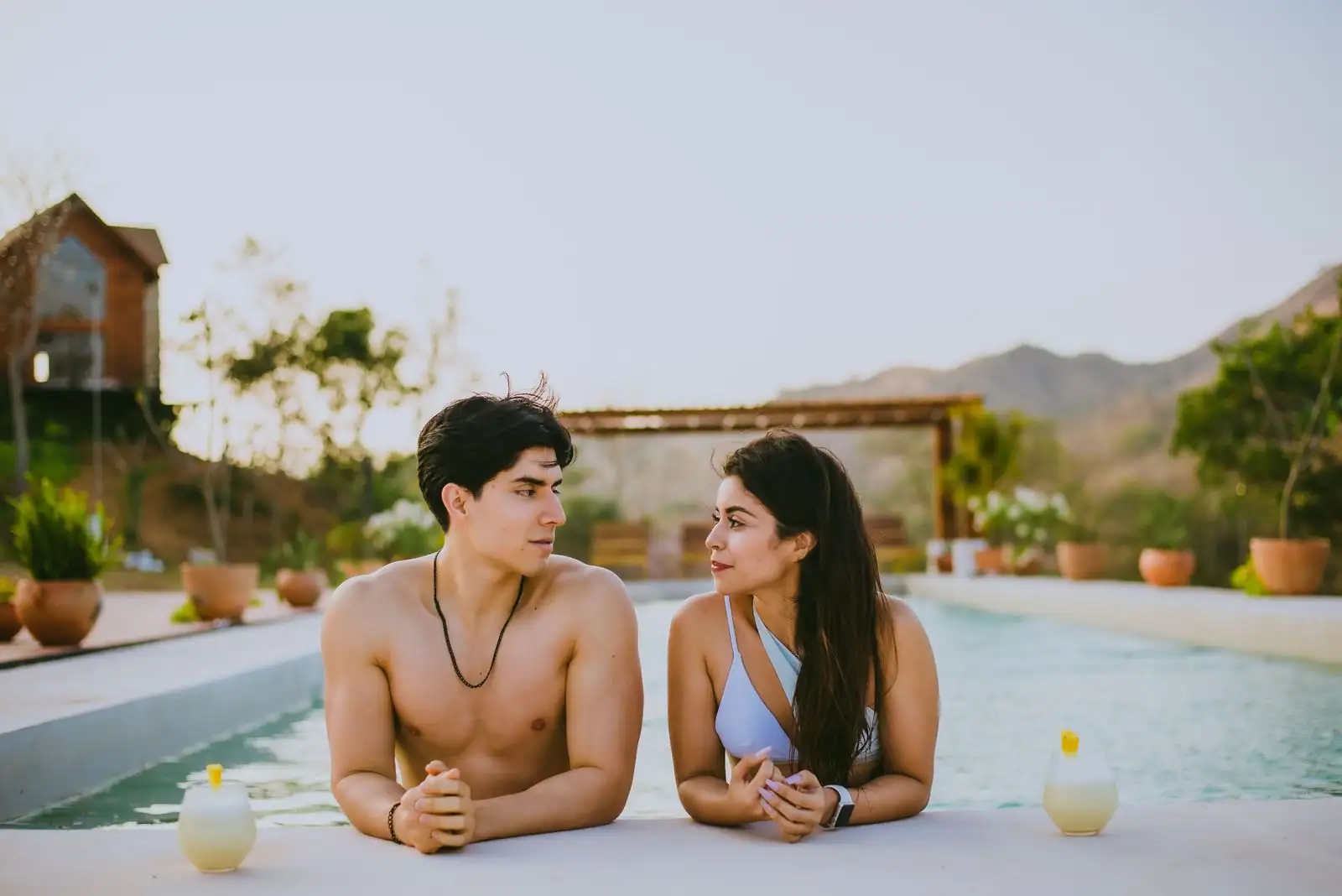 Jeune couple échangeant un regard au bord d'une piscine, dans un décor de vacances ensoleillé.