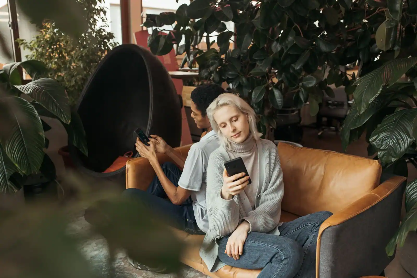 Jeune femme consultant son smartphone, installée sur un canapé dans un intérieur végétalisé.