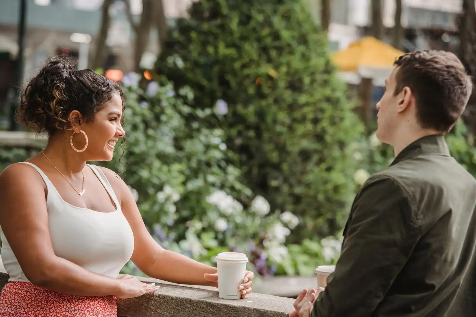 Un homme et une femme échangent en souriant en plein air, un gobelet de café à la main