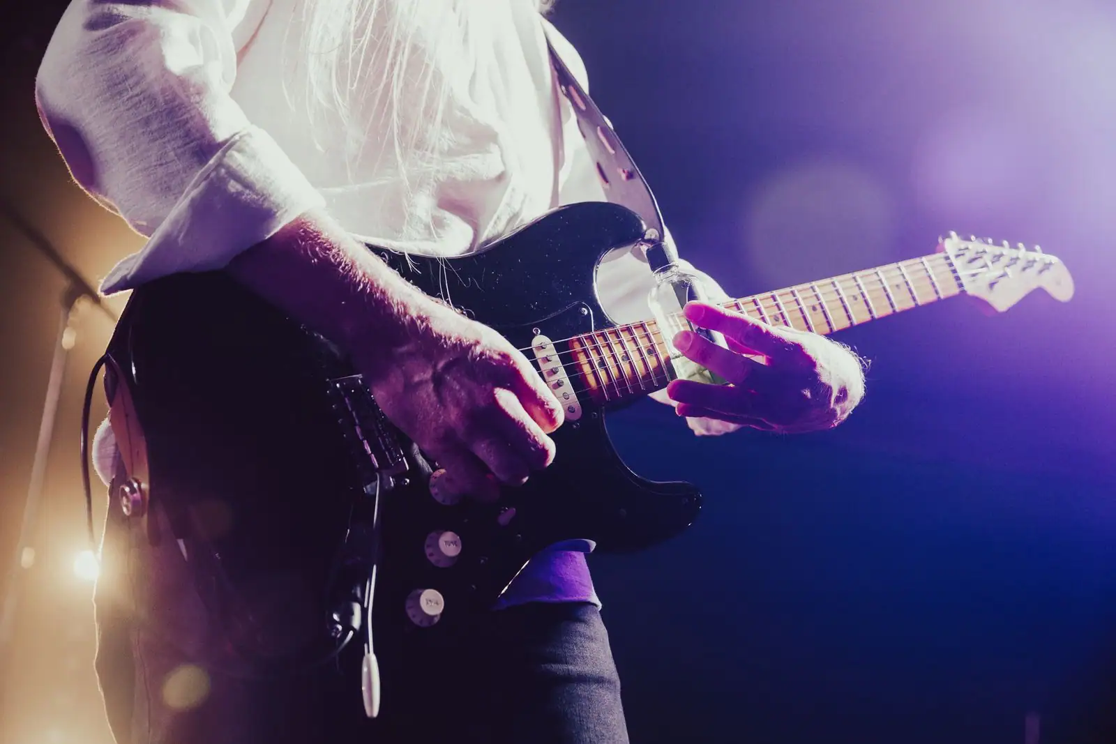 Un guitariste joue une guitare électrique sur scène dans une lumière de concert, en illustration du blues.