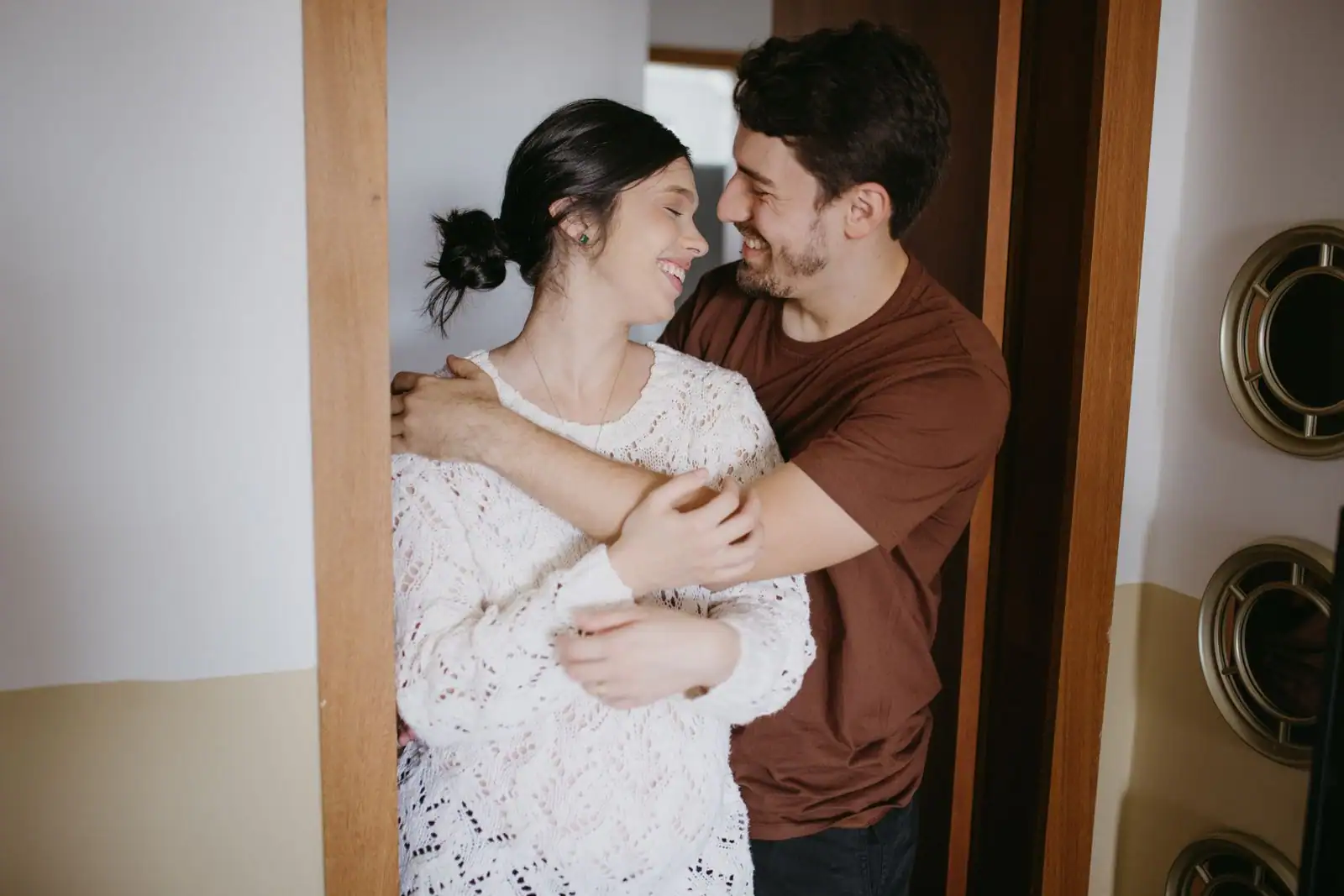 Un couple s'enlace tendrement dans l'encadrement d'une porte, à l'intérieur d'une maison.