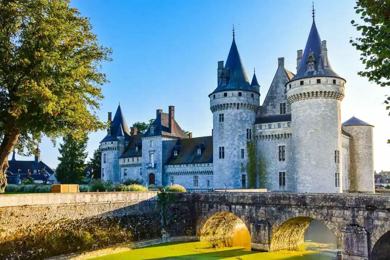 Château français historique en pierre, avec tours à toits coniques et pont enjambant des douves