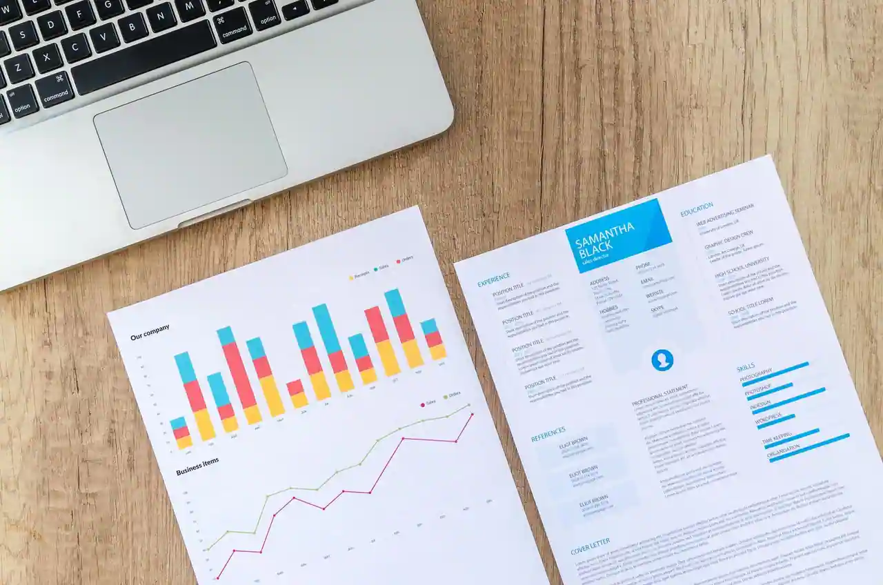 Un curriculum vitae imprimé posé sur un bureau en bois, à côté d'un ordinateur portable et d'une feuille de graphiques.