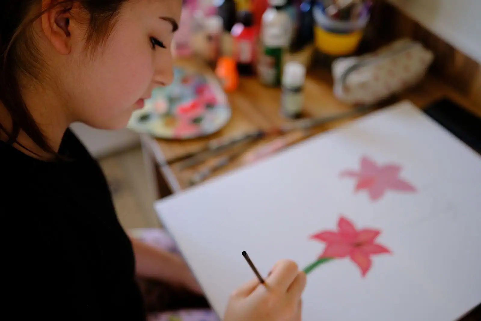 Une jeune femme peint une fleur au pinceau chez elle, palette et couleurs à portée de main, loisir créatif.