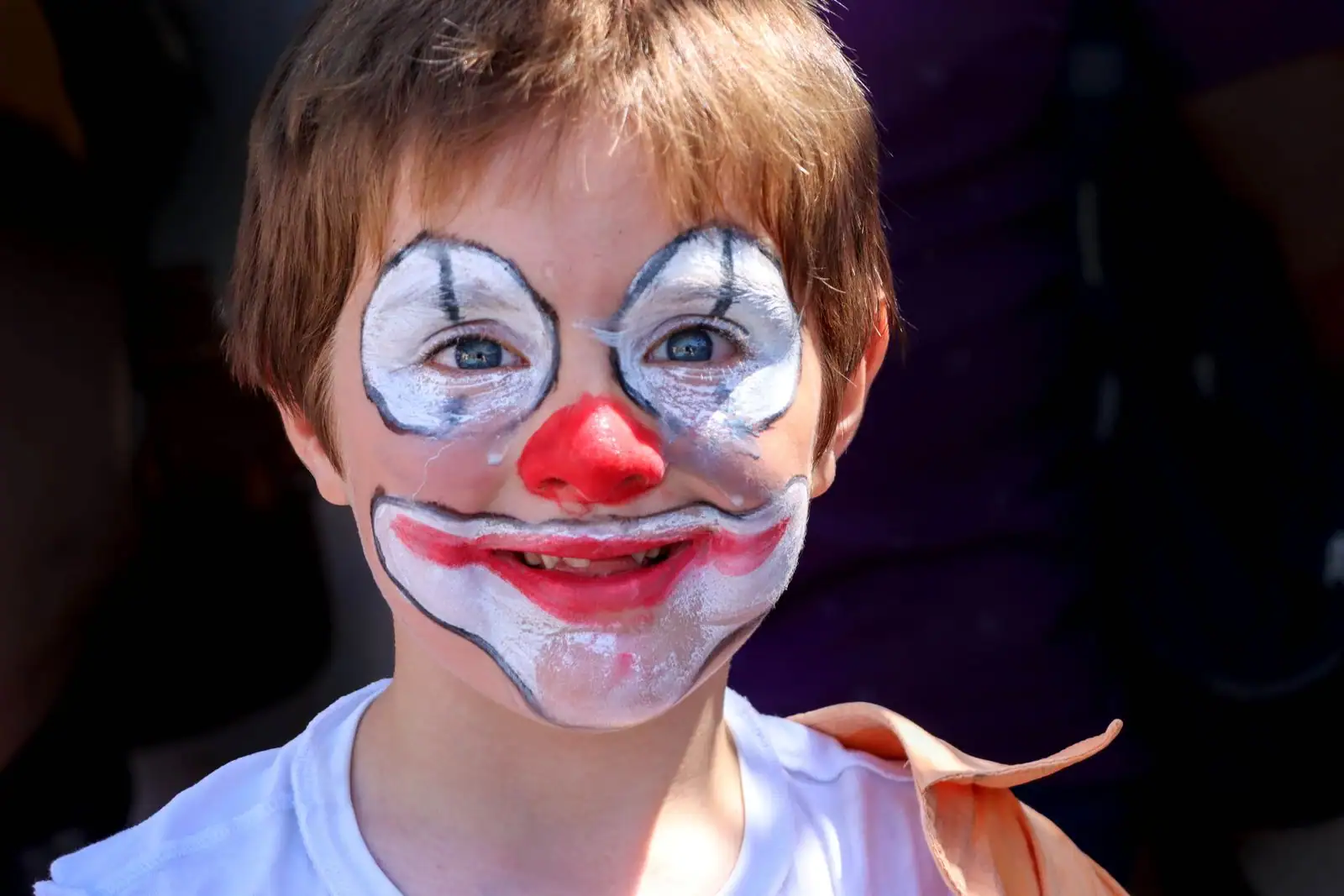 Enfant souriant maquillé en clown gai, base blanche autour des yeux et de la bouche et nez rouge