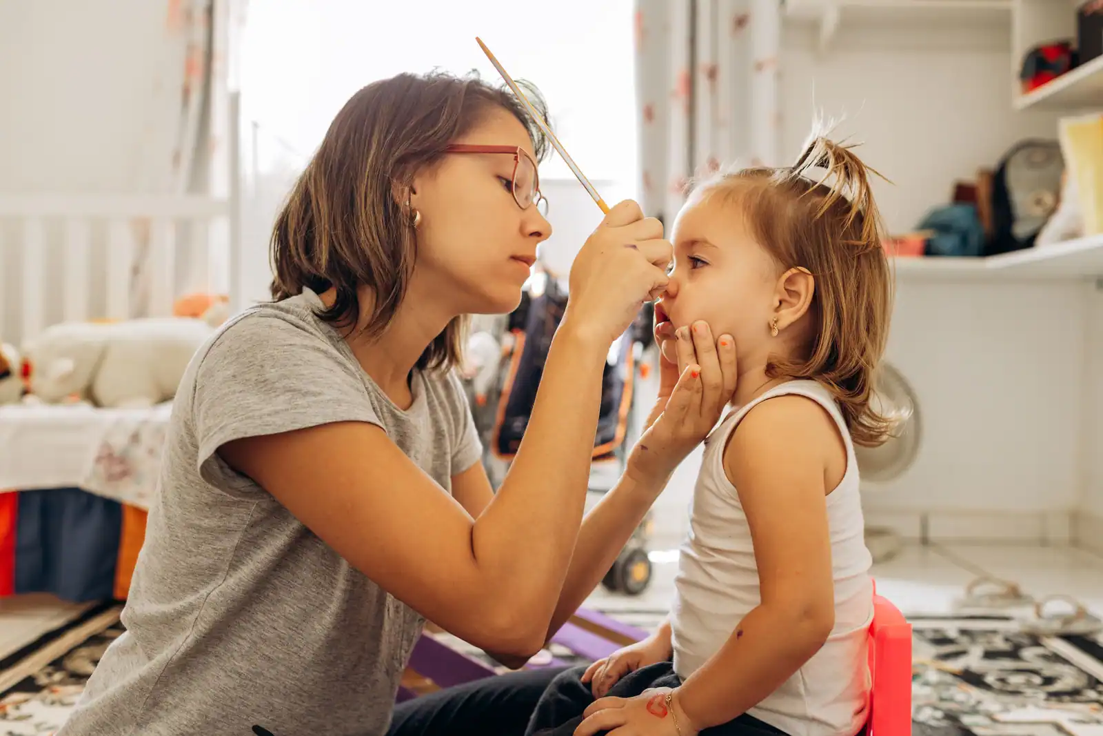 Une femme maquille le visage d'une petite fille au pinceau, lors d'une séance de maquillage enfant