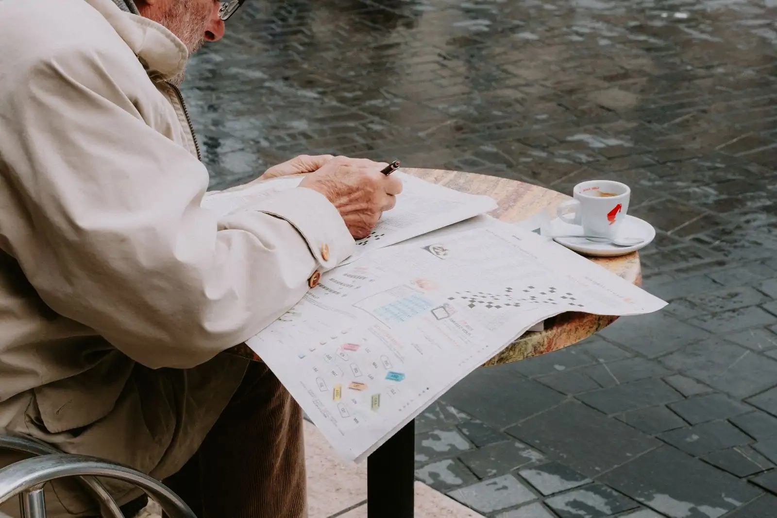 Homme âgé résolvant des mots croisés à la terrasse d’un café, illustrant un passe-temps tranquille du quotidien.