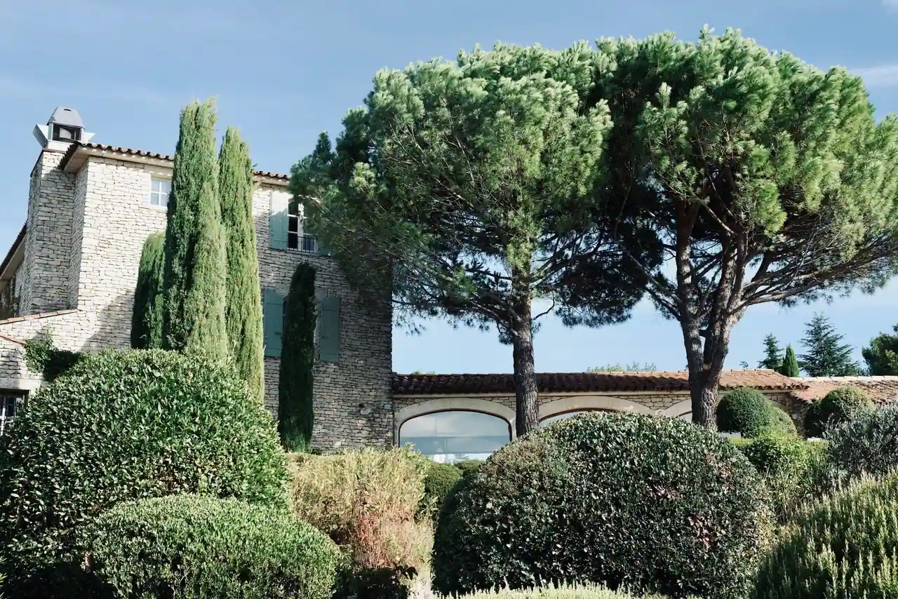 Mas provençal en pierre entouré de cyprès, de pins parasols et de buis taillés sous un ciel bleu