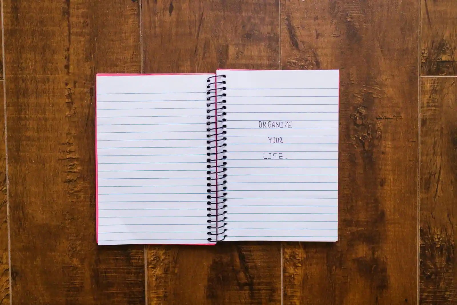 Carnet à spirale ouvert sur un plan de travail en bois, avec une note manuscrite invitant à s'organiser.