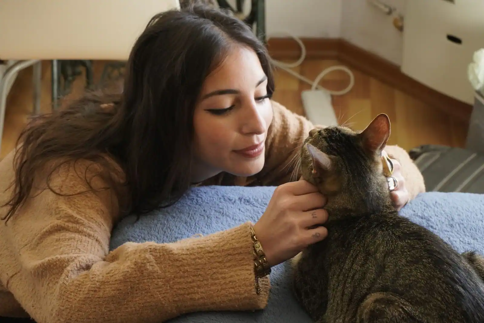 Une jeune femme en pull beige caresse tendrement son chat tigré dans un intérieur cosy.