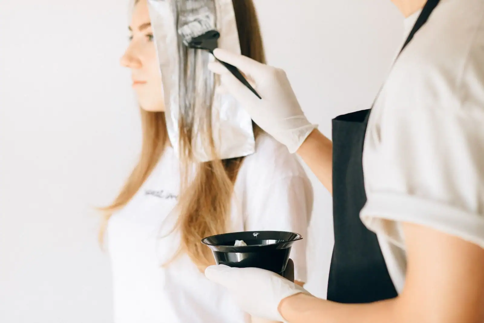En salon, une coiffeuse applique la couleur au pinceau sur les mèches d’une cliente.