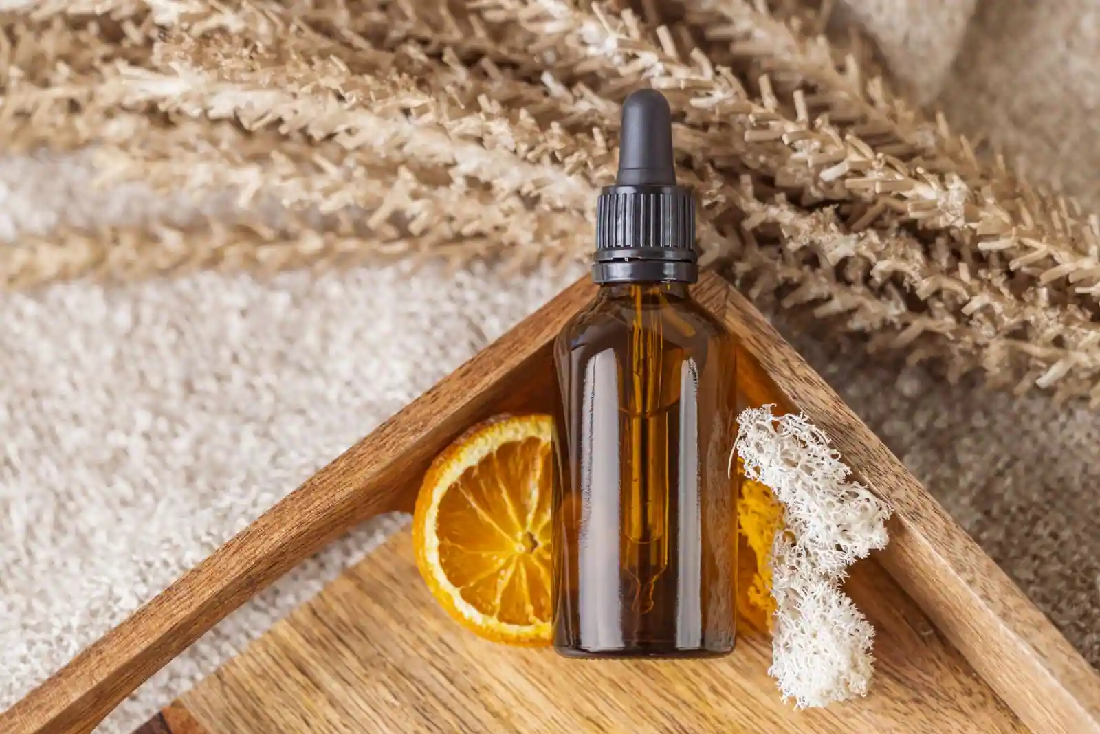 Un flacon de soin cosmétique bio à pipette, posé sur un plateau en bois avec des végétaux séchés.