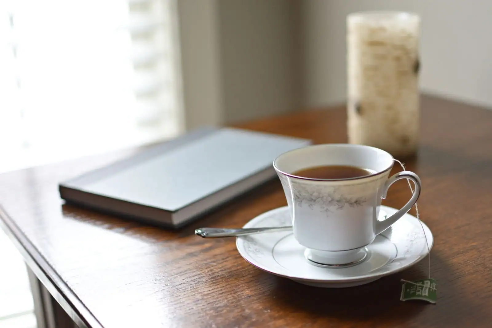 Tasse de thé, carnet et bougie sur une table en bois près d'une fenêtre, lumière matinale