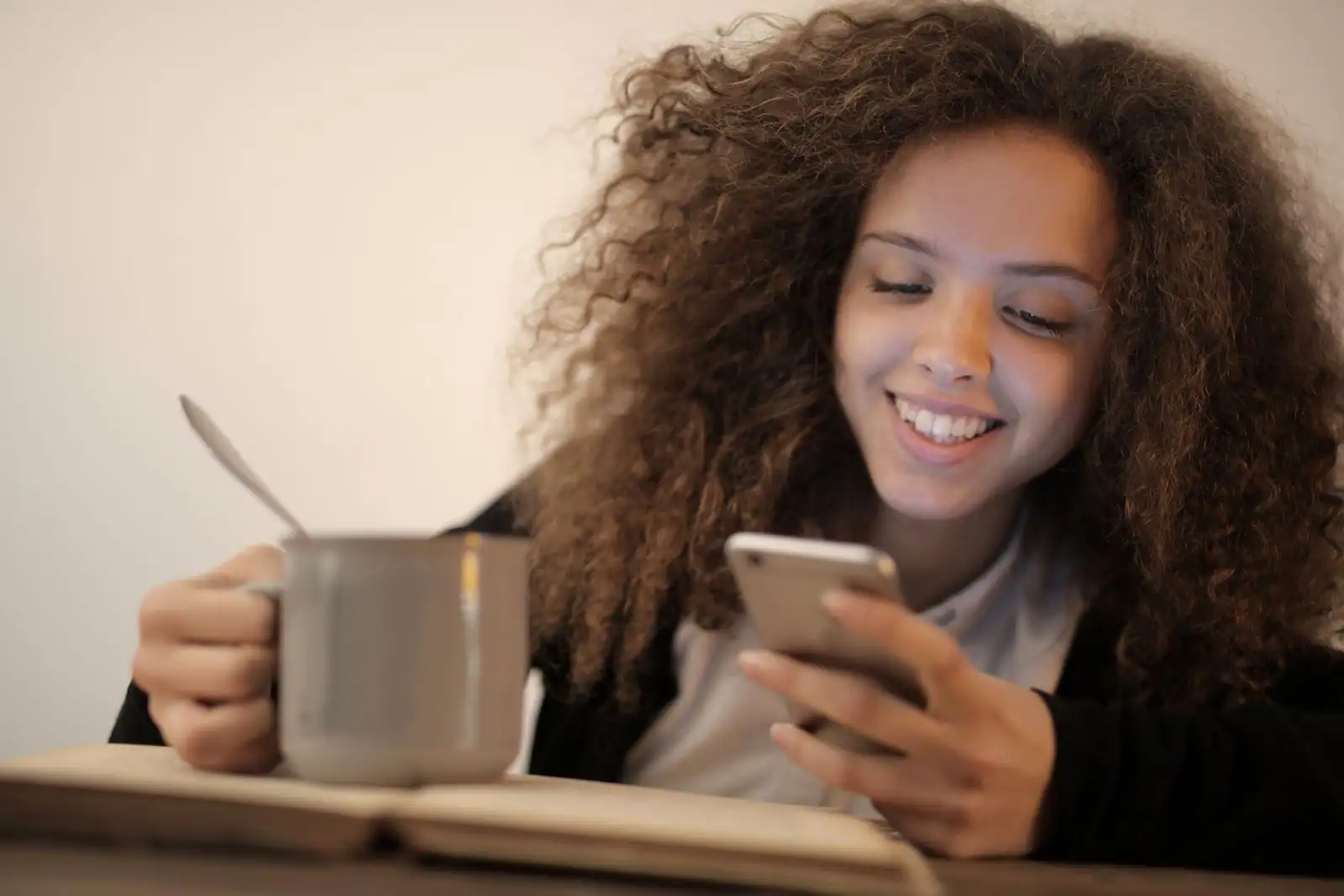 Jeune femme souriante lisant un message sur son smartphone, installée dans un intérieur clair et paisible