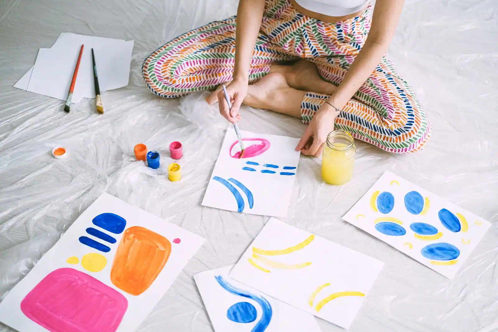 Personne assise au sol peignant des motifs colorés sur des feuilles, une activité de loisir créative