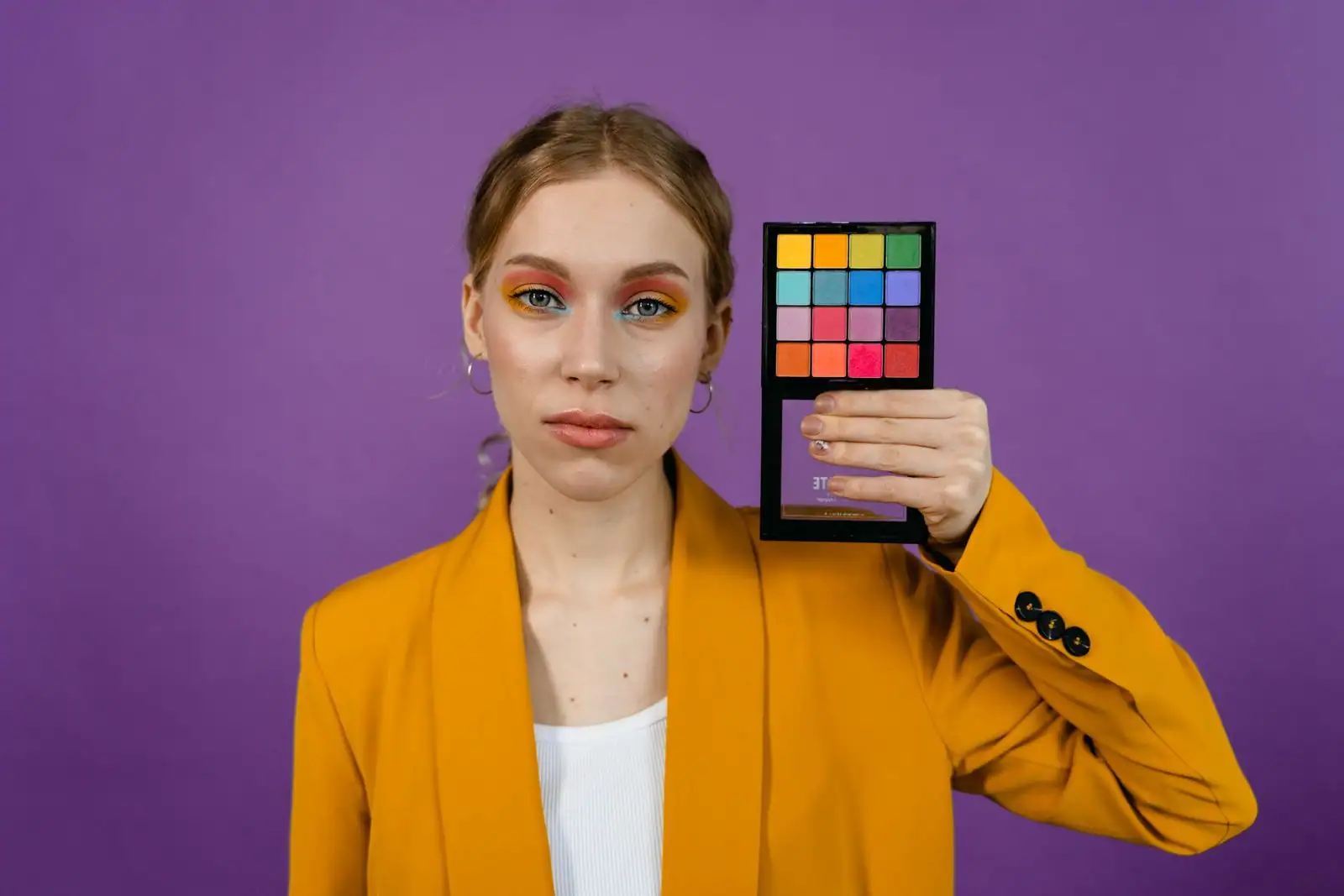 Femme au maquillage coloré aux fards vifs, tenant une palette d'ombres à paupières multicolore