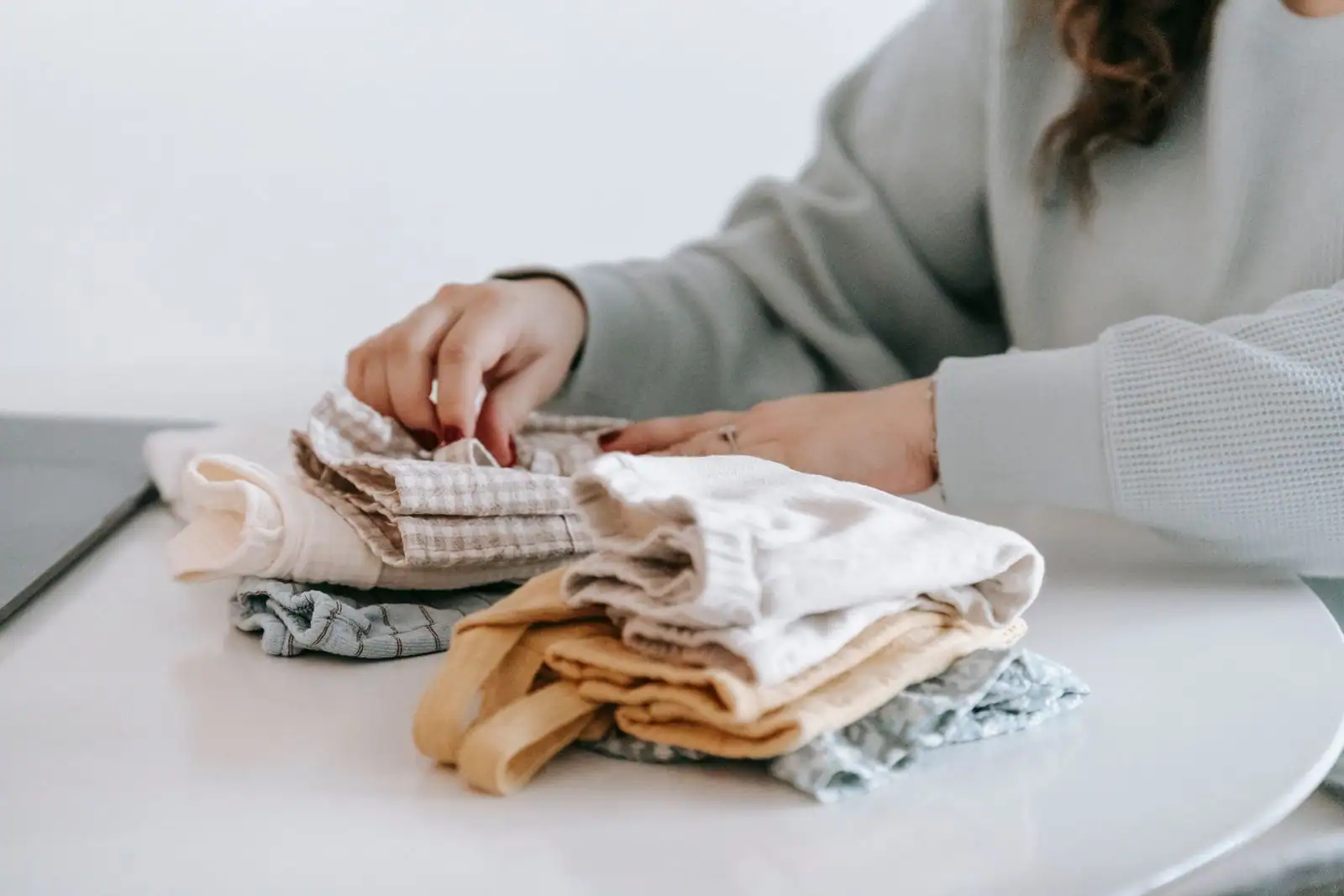Une personne plie et trie une pile de vêtements et de linge posés sur une table claire.