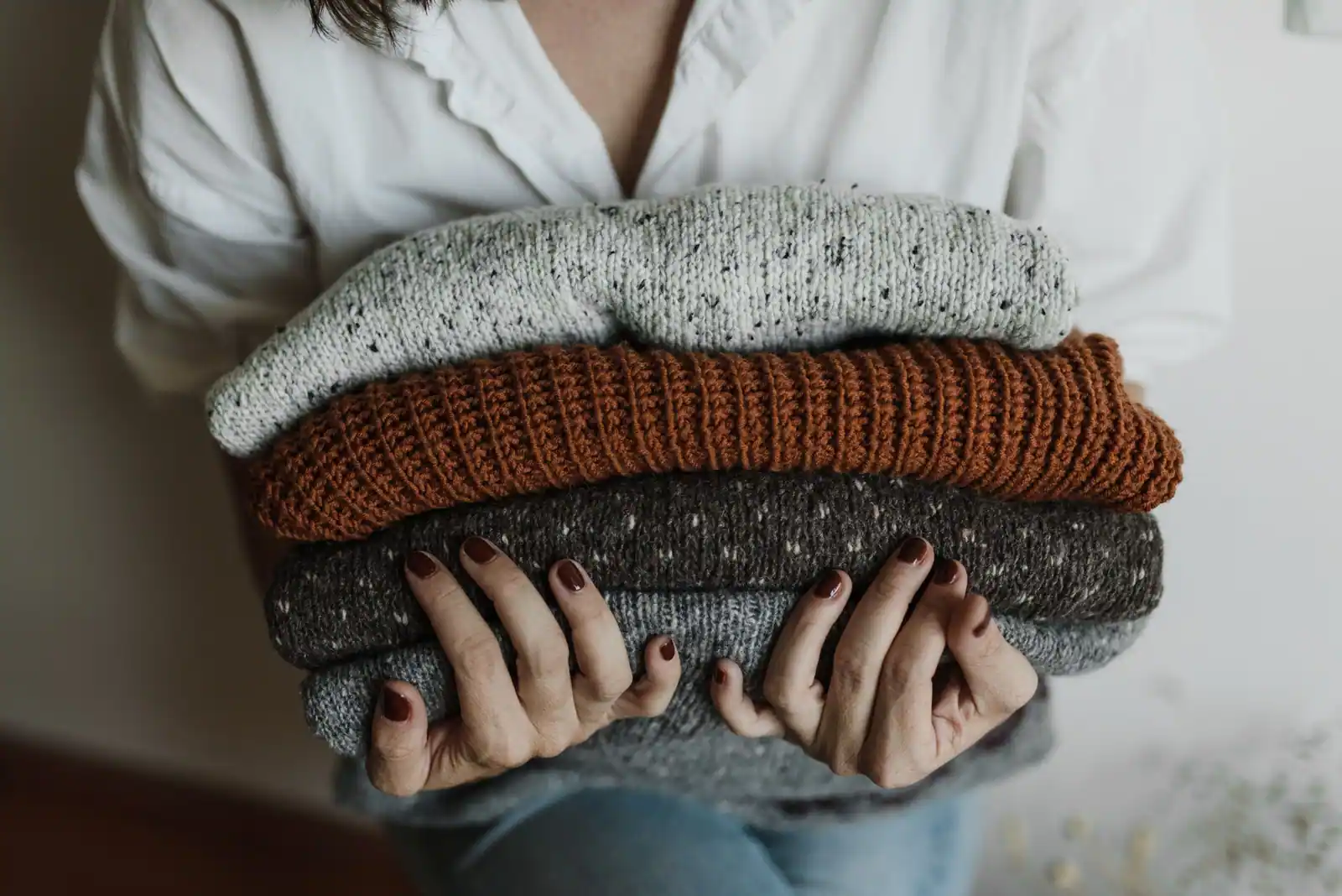 Pile de pulls en maille tenue dans les bras : vert d'eau moucheté, rouille et gris chinés