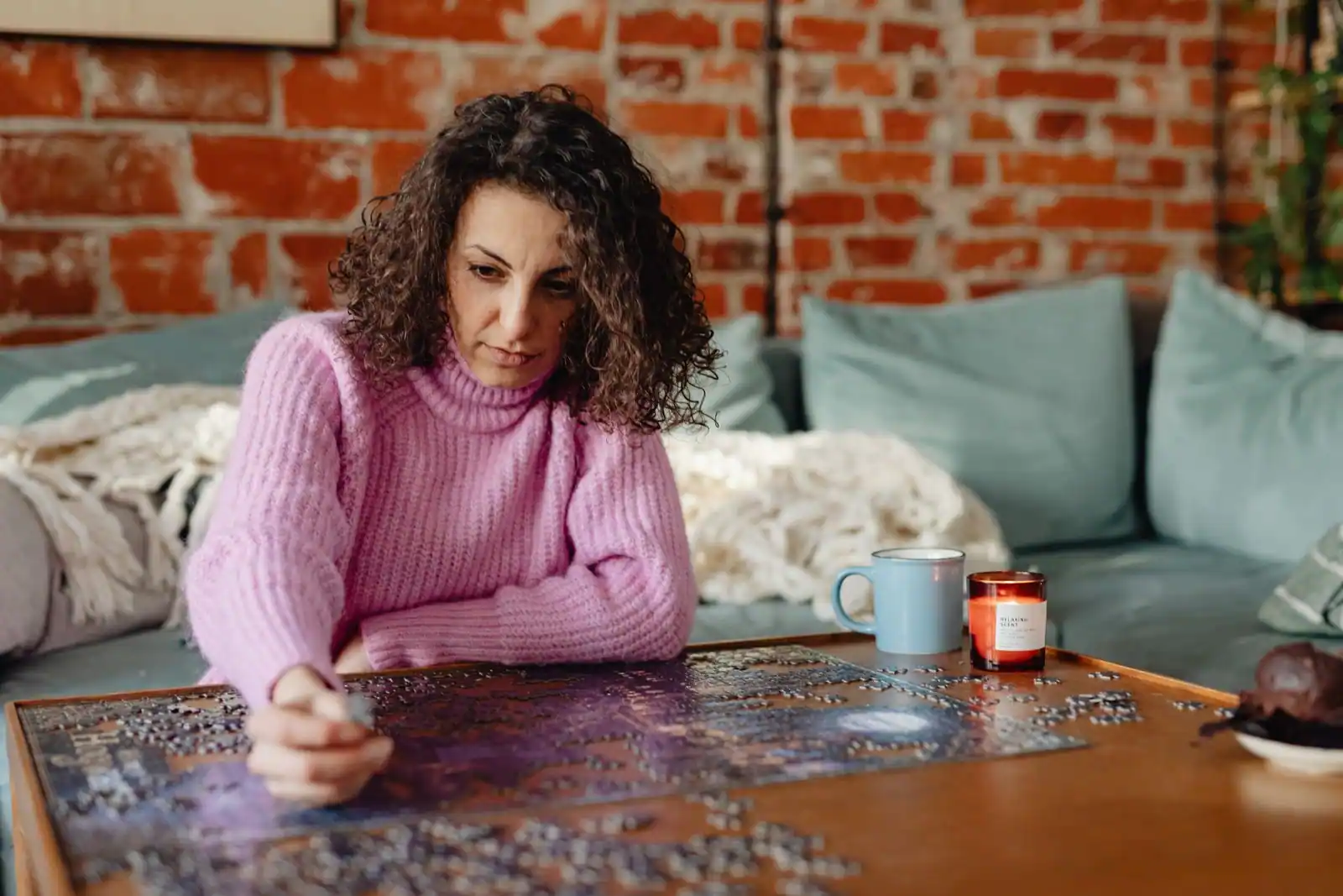 Une femme assemble les pièces d'un puzzle sur une table en bois, dans un moment de loisir tranquille.