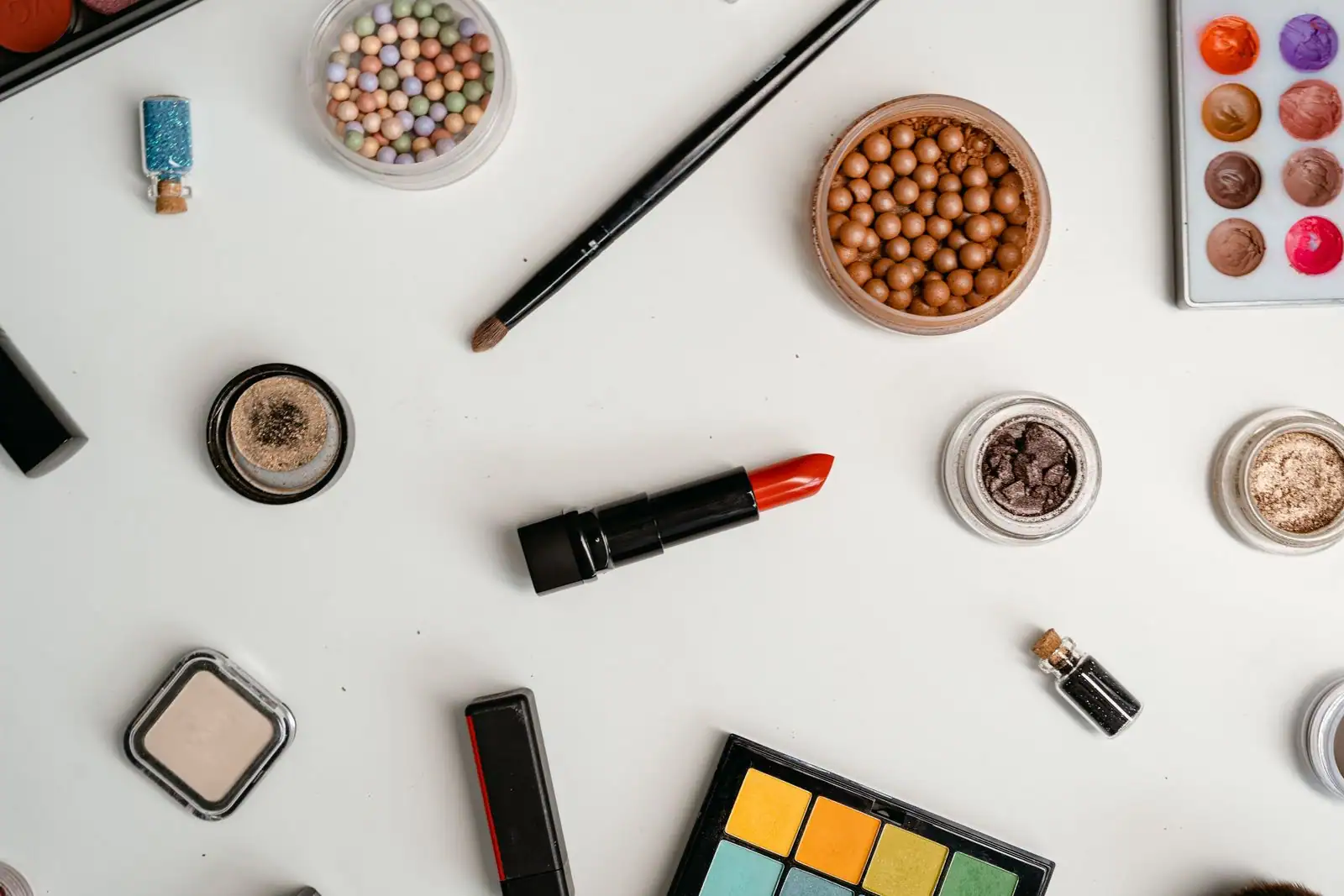 Produits de maquillage à plat sur fond blanc : pinceau, rouge à lèvres, palettes de fards et poudres