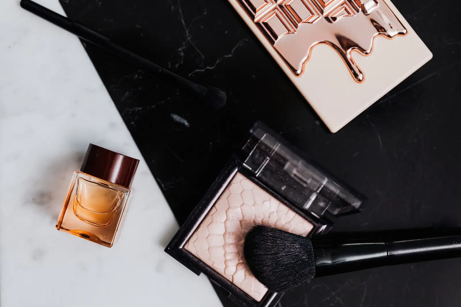Palette de fards nude, poudre illuminatrice, pinceaux et flacon de parfum posés sur un plan en marbre