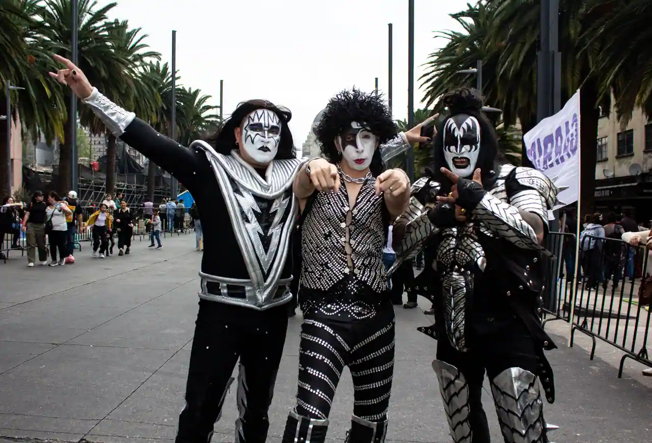 Trois personnes maquillées et costumées en membres du groupe KISS posant dans une rue animée