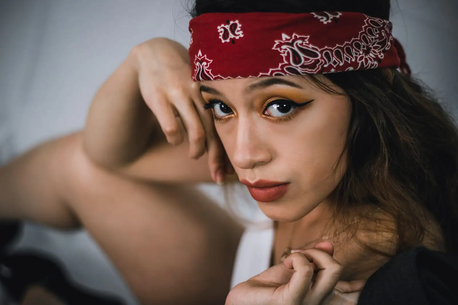 Portrait rapproché d'une femme au bandana rouge : trait d'œil noir graphique, fard doré et bouche rouge