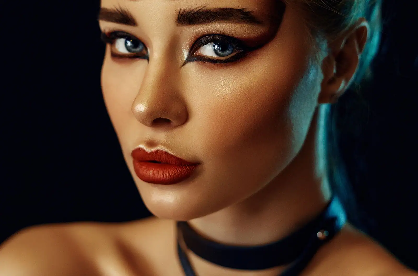 Femme au teint bronzé sculpté, sourcils denses et bouche rouge brique mate, regard souligné de noir