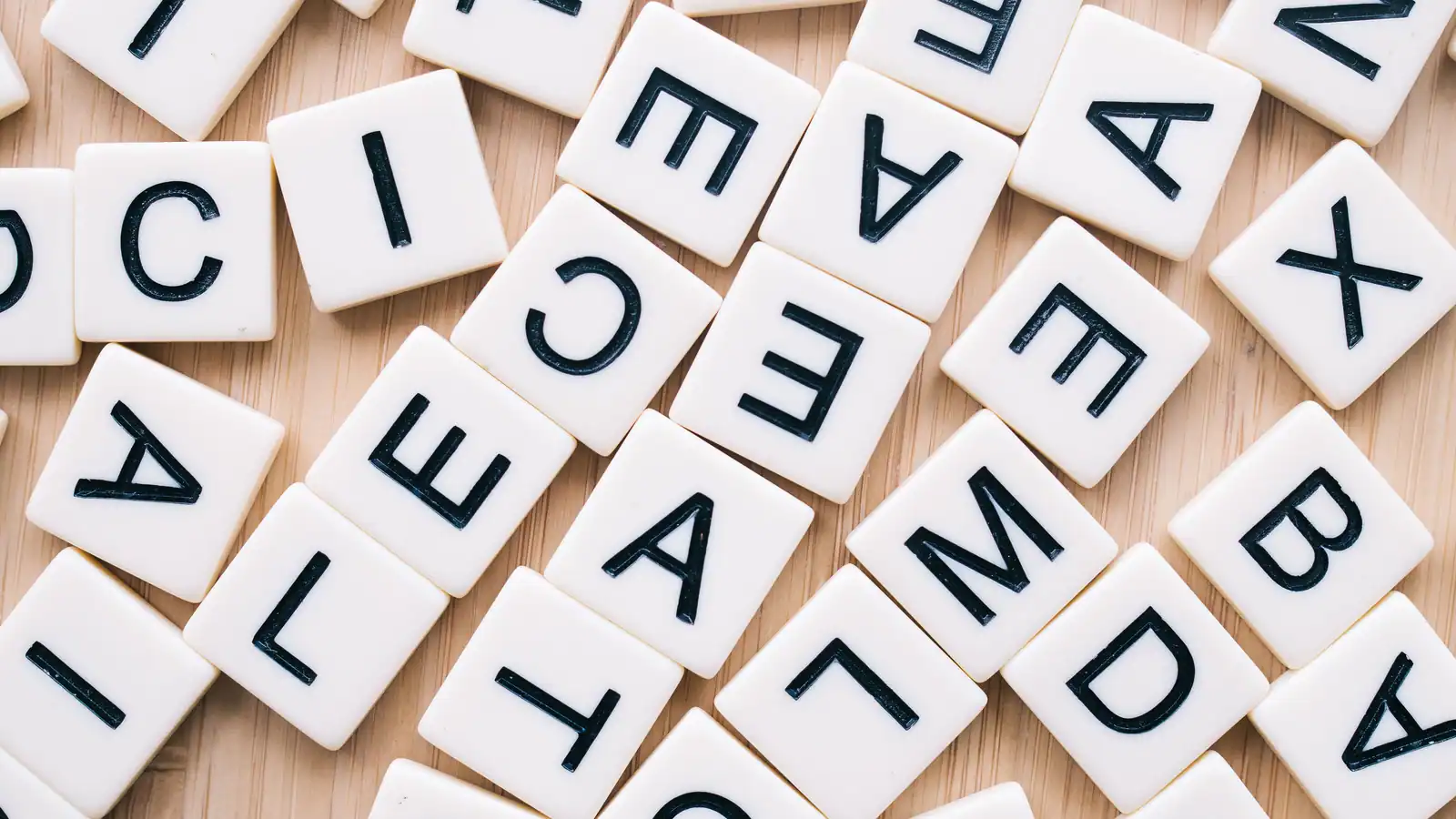 Jetons de lettres blancs éparpillés sur une table en bois clair, vus du dessus, sans mot formé