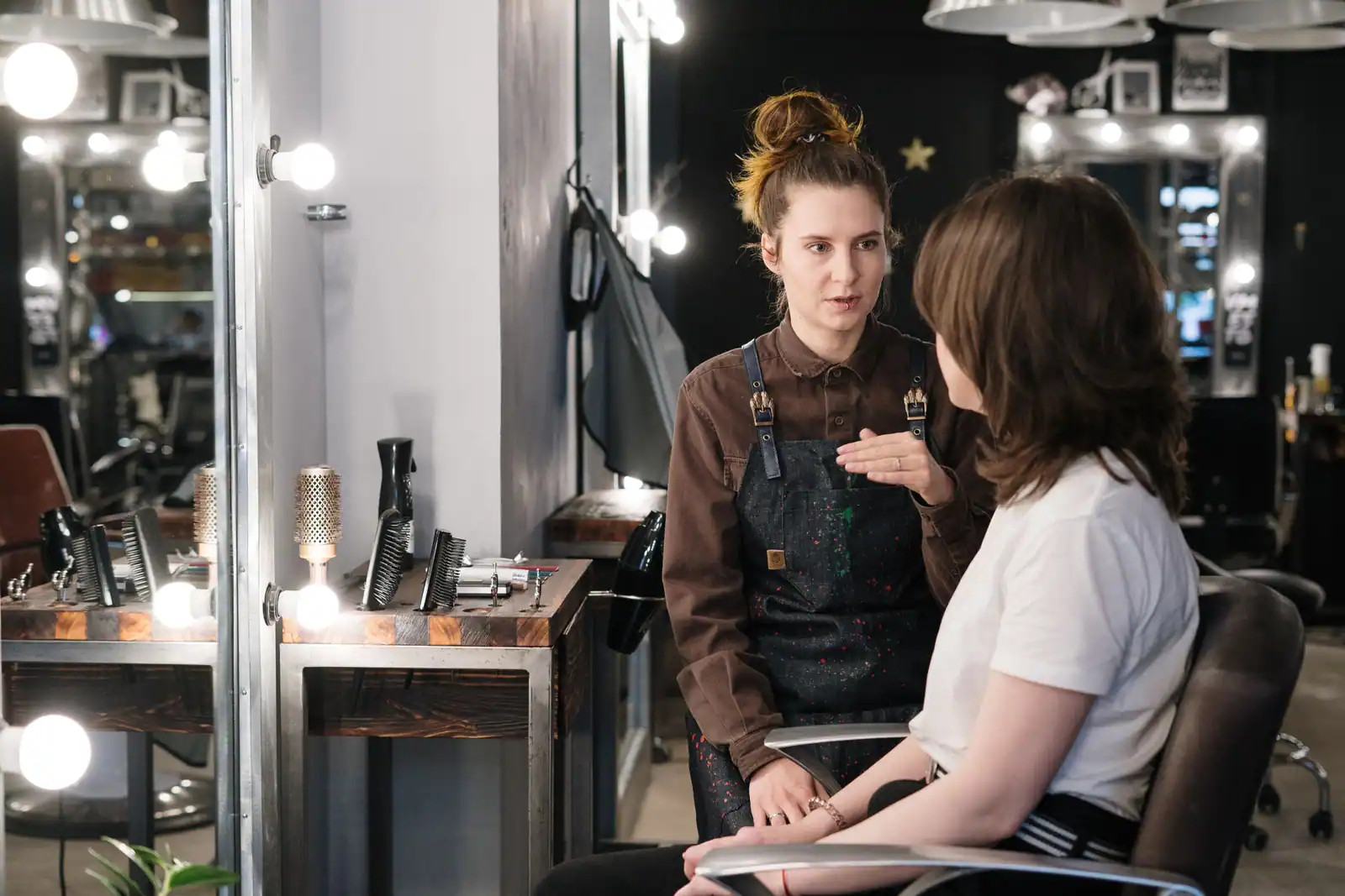 En salon, une coiffeuse échange avec sa cliente installée dans le fauteuil, au moment du diagnostic préalable.